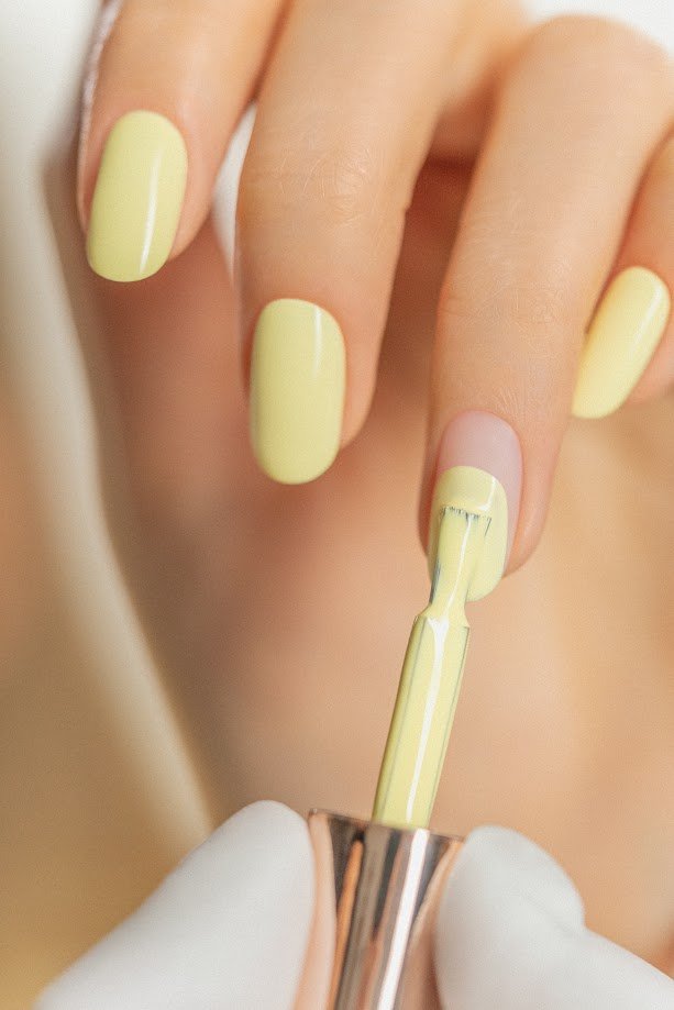 Kobieta maluje paznokcie na żółot lakierem Lemonidas Indigo Nails - wiosenne trendy
